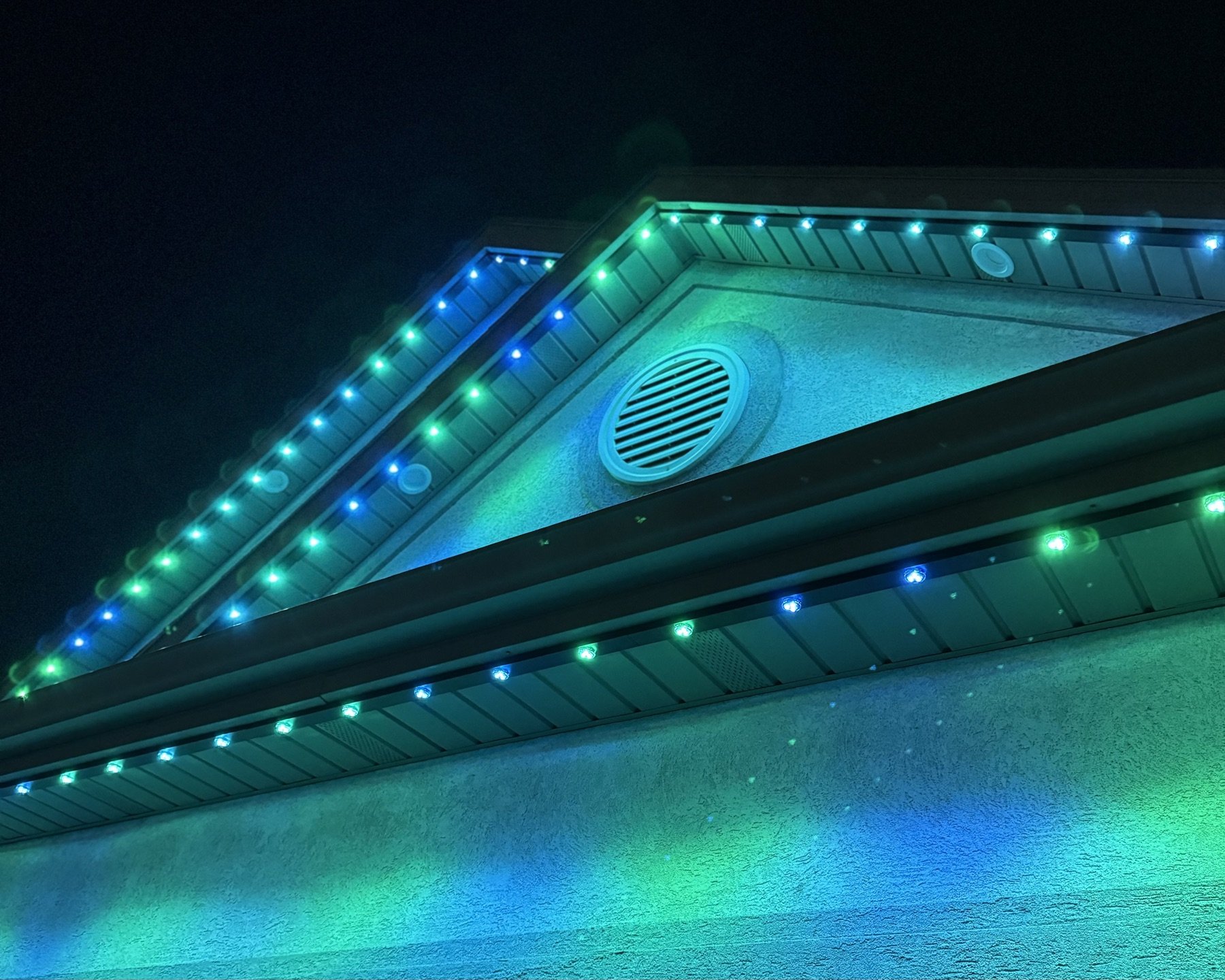 Green and blue lighting along a home’s gable